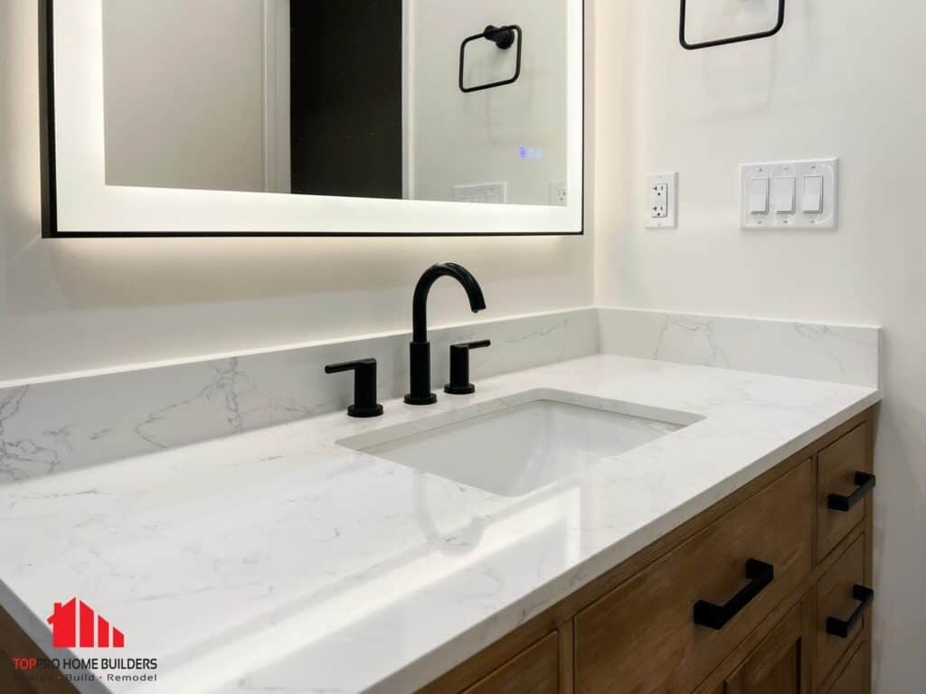 Bathroom vanity with marble countertop, black fixtures, and illuminated mirror.