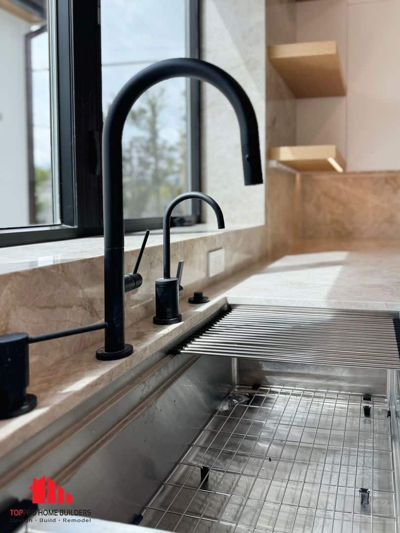 Modern kitchen sink with black faucets and marble countertop.