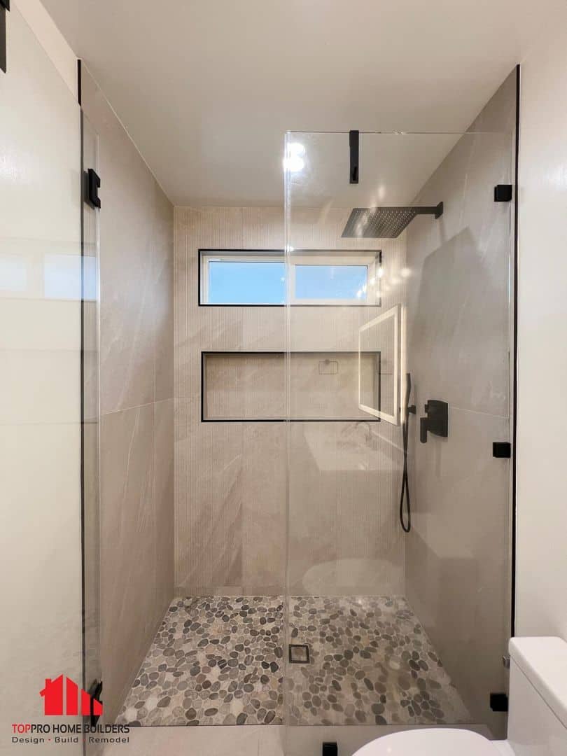 Image of a modern bathroom shower with glass doors and pebble flooring.