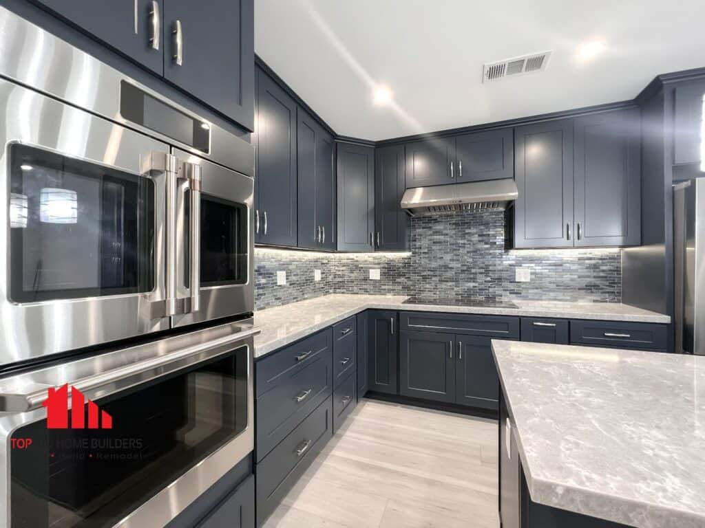 Modern kitchen with dark blue cabinets, stainless steel appliances, and mosaic backsplash.