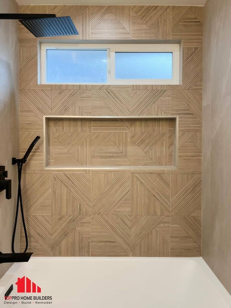 Image of a modern bathroom shower with geometric tiles, a recessed shelf, and black fixtures.