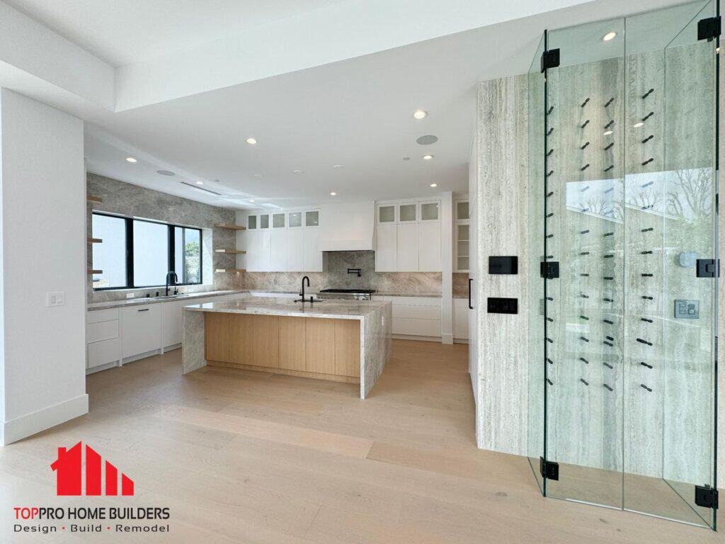 Image of a modern kitchen with an island, white cabinets, and glass wine storage.