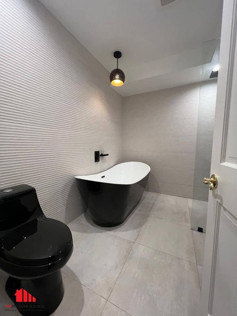 Modern bathroom with black bathtub and toilet, textured walls, and pendant lighting.