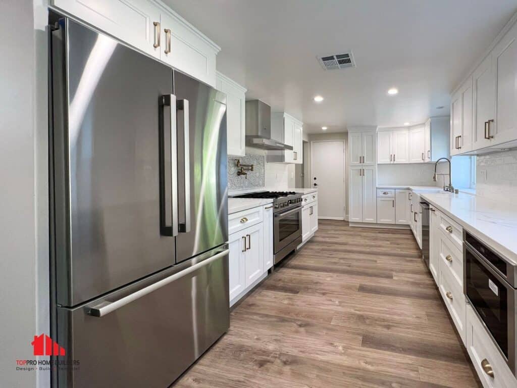 Image of a modern kitchen with stainless steel fridge, white cabinets, and hardwood floors.