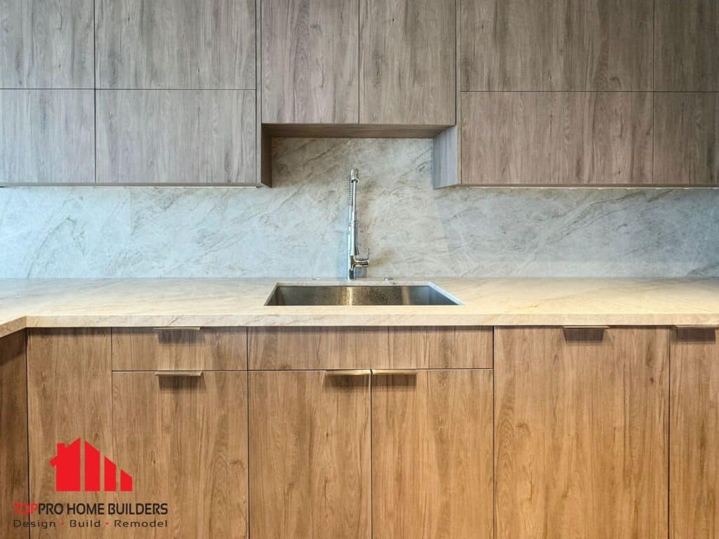 Modern kitchen with wooden cabinets, stainless steel sink, and marble backsplash by TopPro Home Builders.