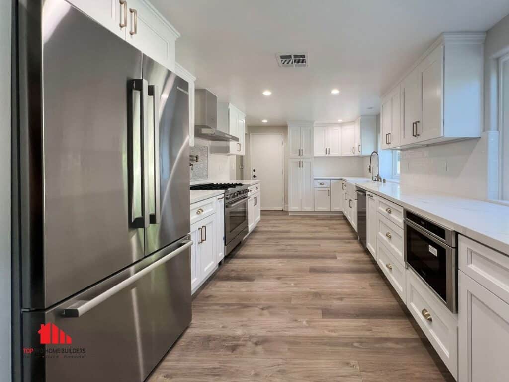 Image of a remodeled kitchen with stainless steel refrigerator, white cabinets, and wooden flooring.