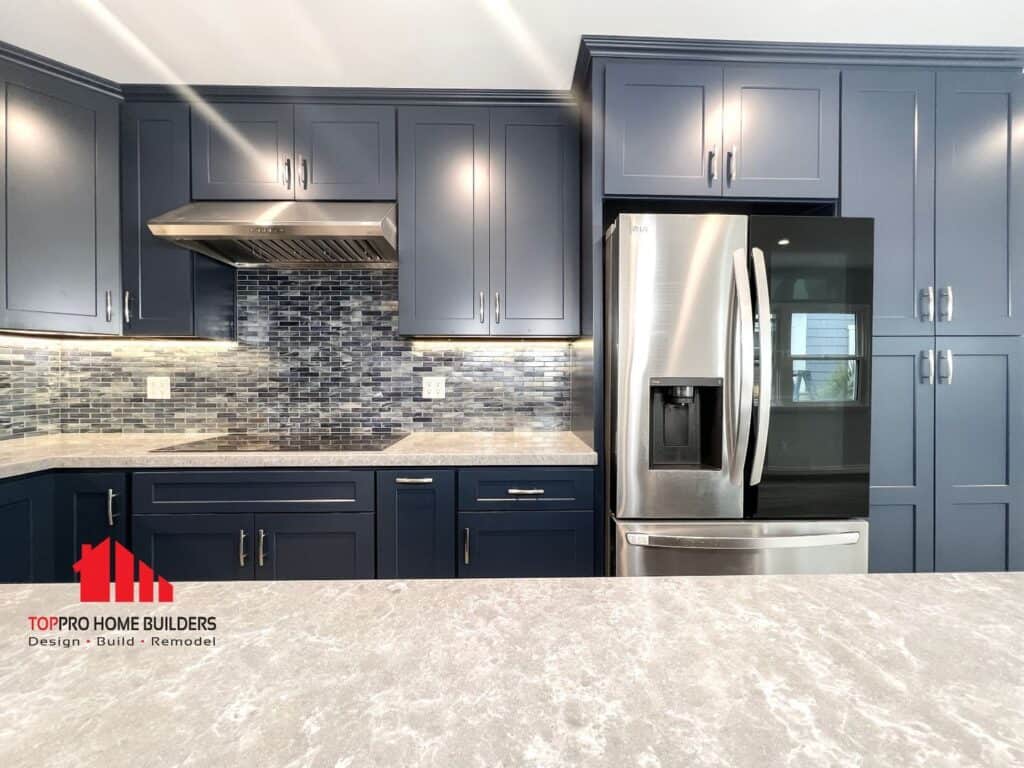 Modern kitchen with dark blue cabinets, stainless steel fridge, and mosaic tile backsplash.