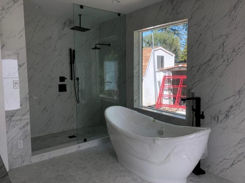 Bathroom with freestanding tub, marble walls, and glass shower enclosure.