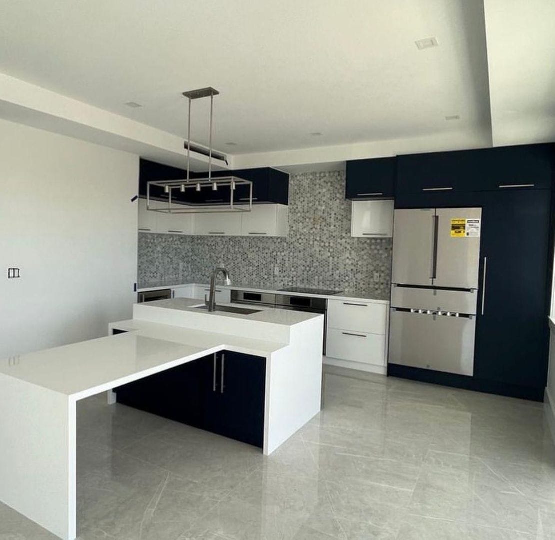 Modern kitchen with central island, dark blue and white cabinets, and stainless steel appliances.