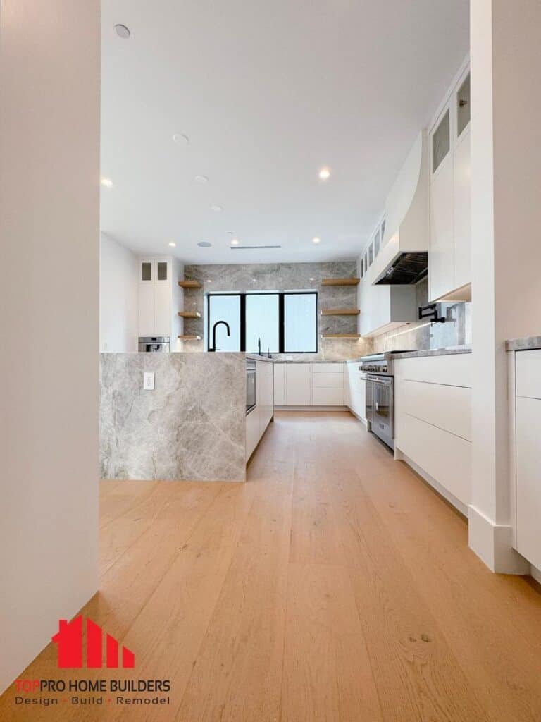 Image of a modern kitchen with white cabinets, marble countertops, and stainless steel appliances.