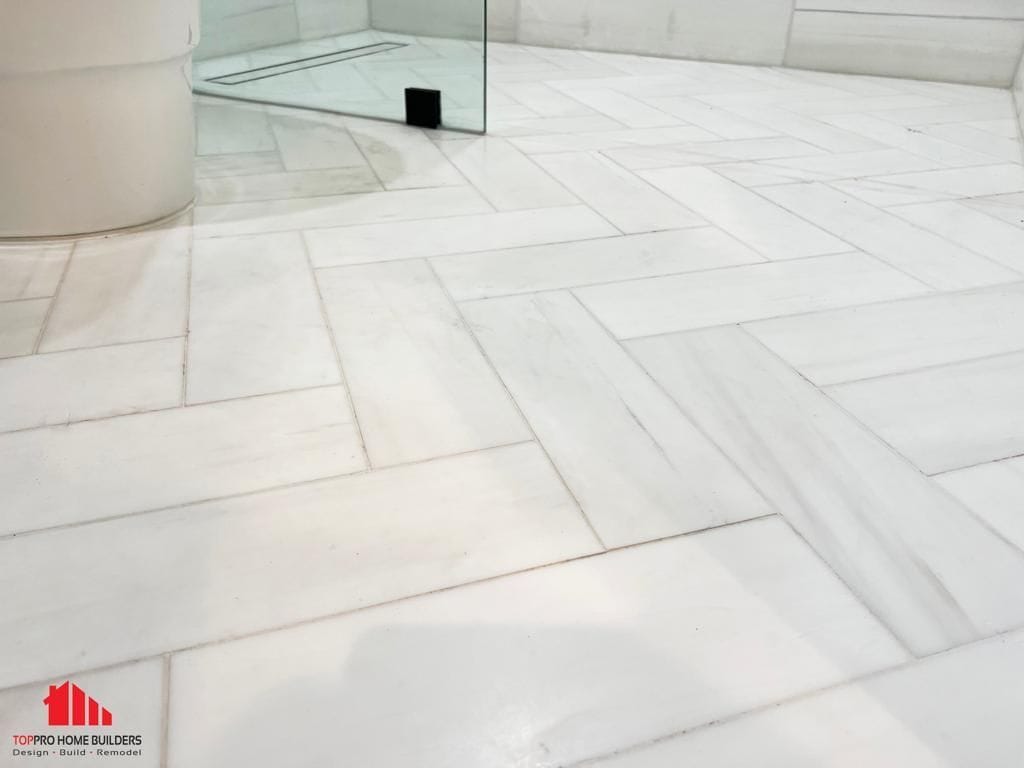 Bathroom floor with white herringbone tiles and glass shower enclosure.