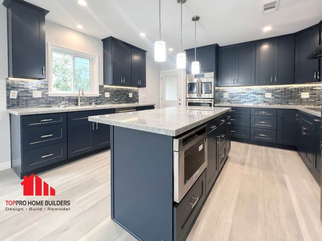 Modern kitchen with dark blue cabinets, marble countertops, and pendant lighting.