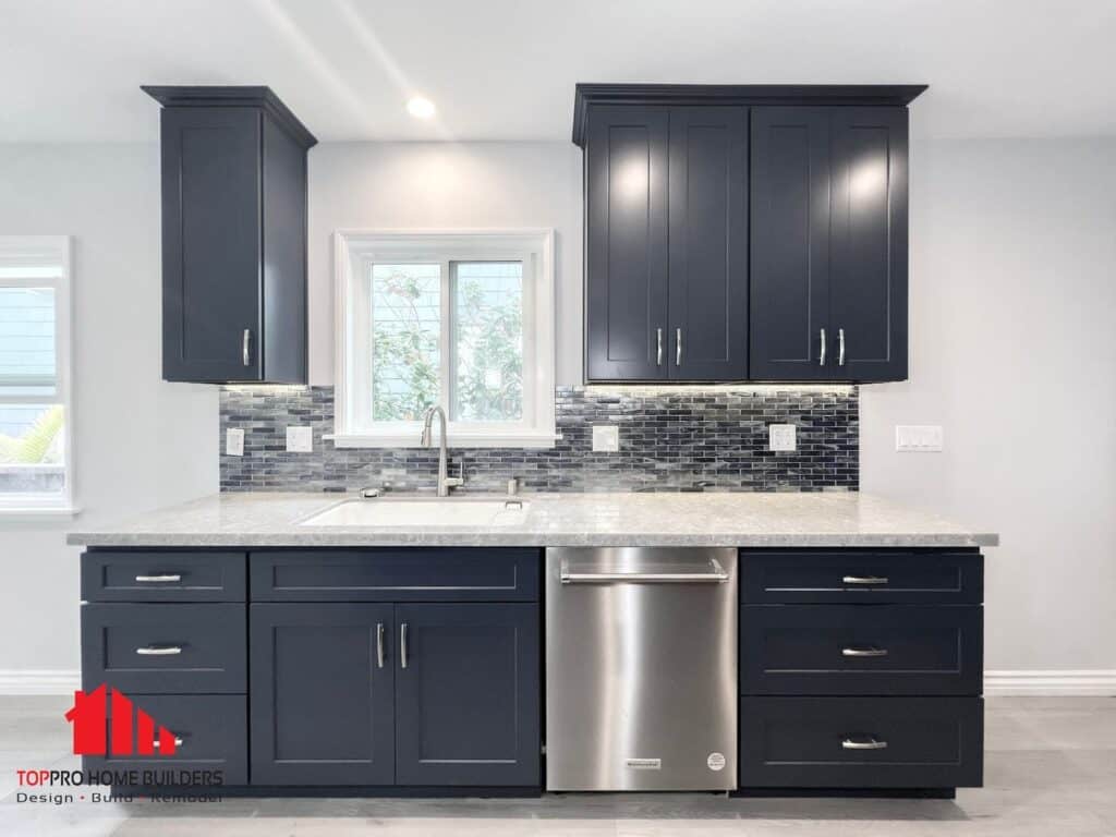 Modern kitchen with dark blue cabinets, stainless steel dishwasher, and tile backsplash.