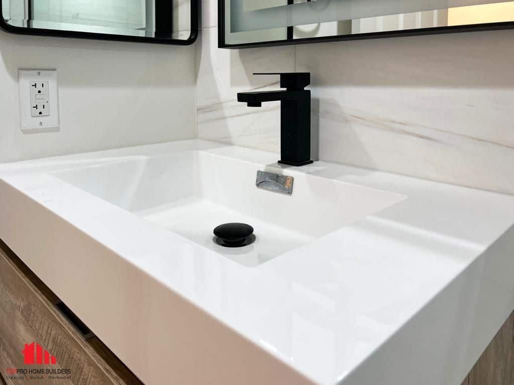 Modern white sink with black faucet and marble backsplash in a remodeled bathroom.