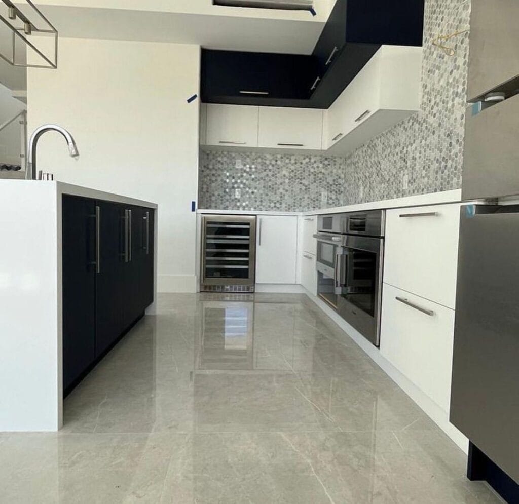 Modern kitchen with navy and white cabinets, stainless steel appliances, and mosaic backsplash.