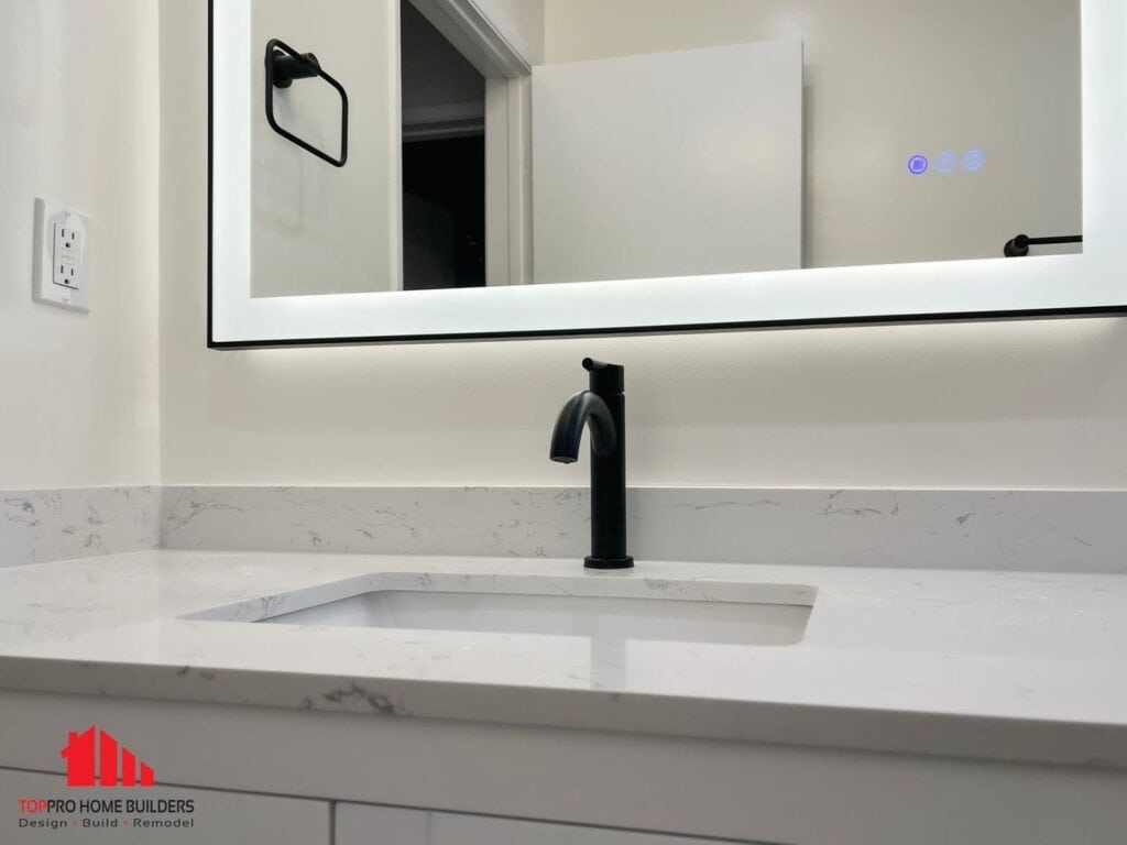 Bathroom sink area with black faucet and illuminated mirror.