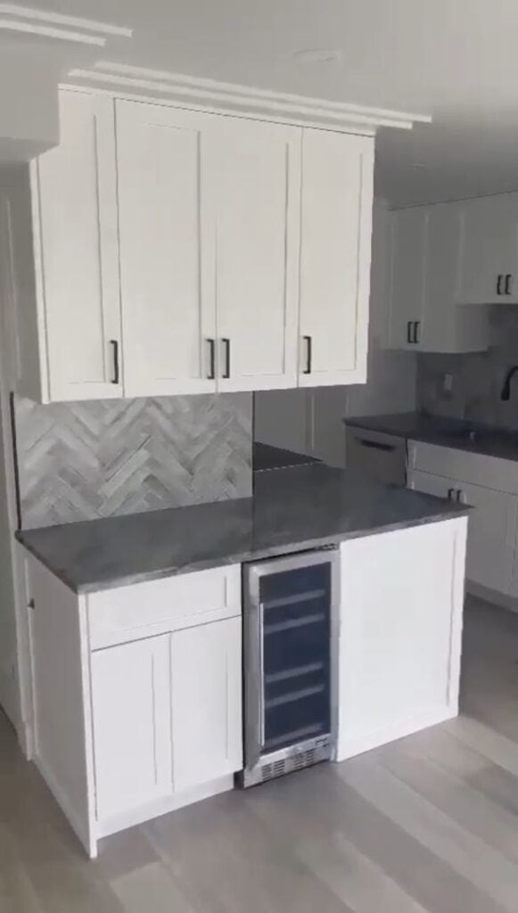 Modern kitchen with white cabinets, herringbone backsplash, and wine cooler.