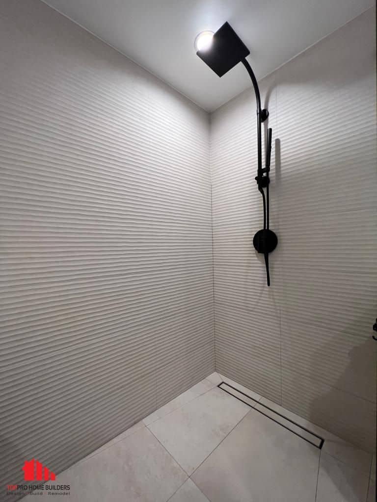 Shower area with textured tiles and black fixtures in a remodeled bathroom.