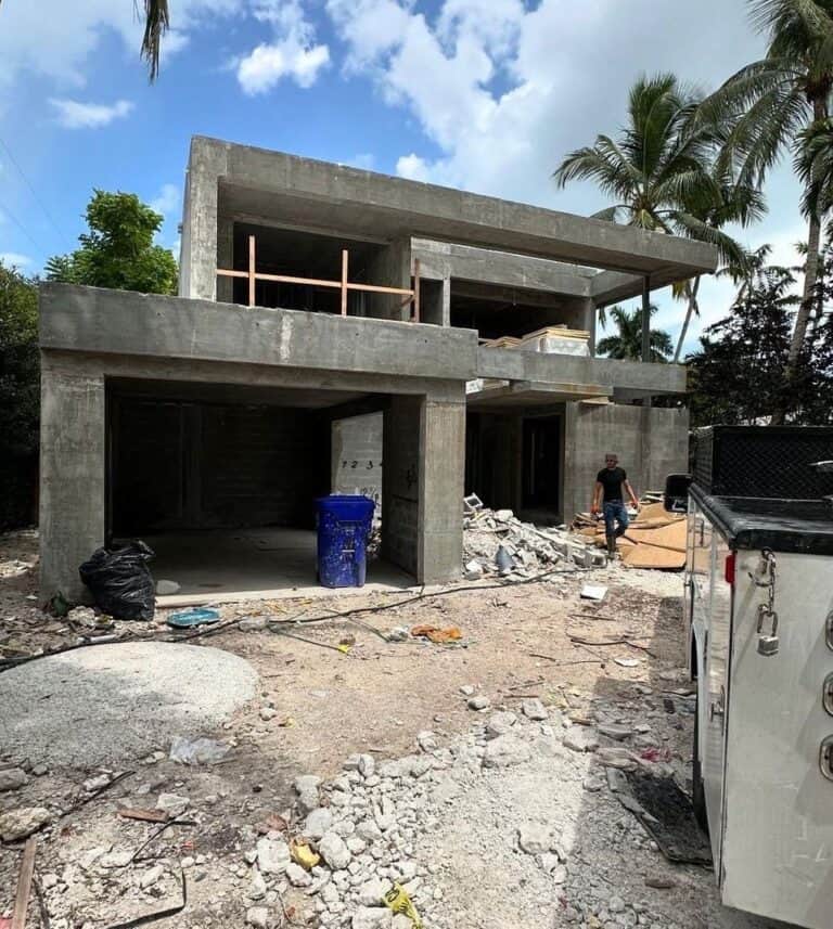 Concrete house under construction with debris and palm trees around.