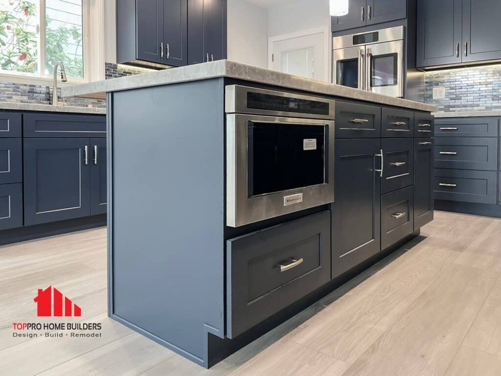 Image of a modern kitchen with navy blue cabinets, stainless steel appliances, and light gray countertops.