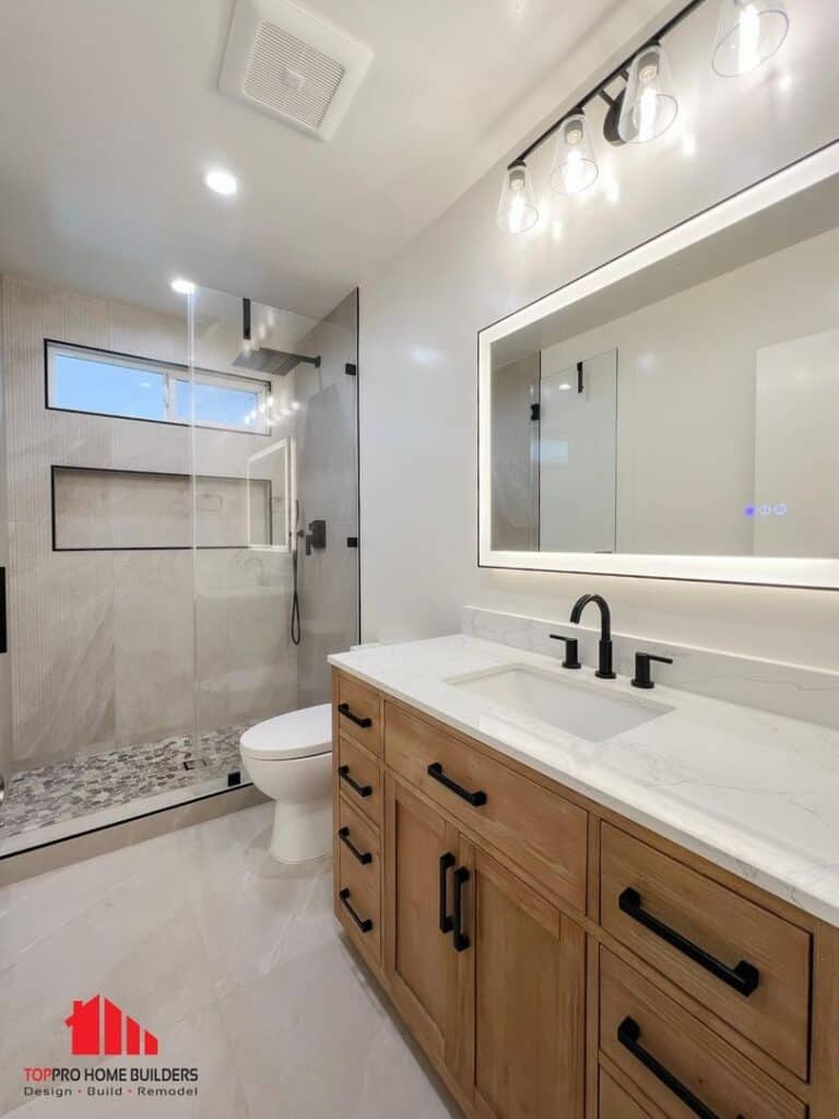 Modern bathroom with glass shower, wooden vanity, and illuminated mirror.