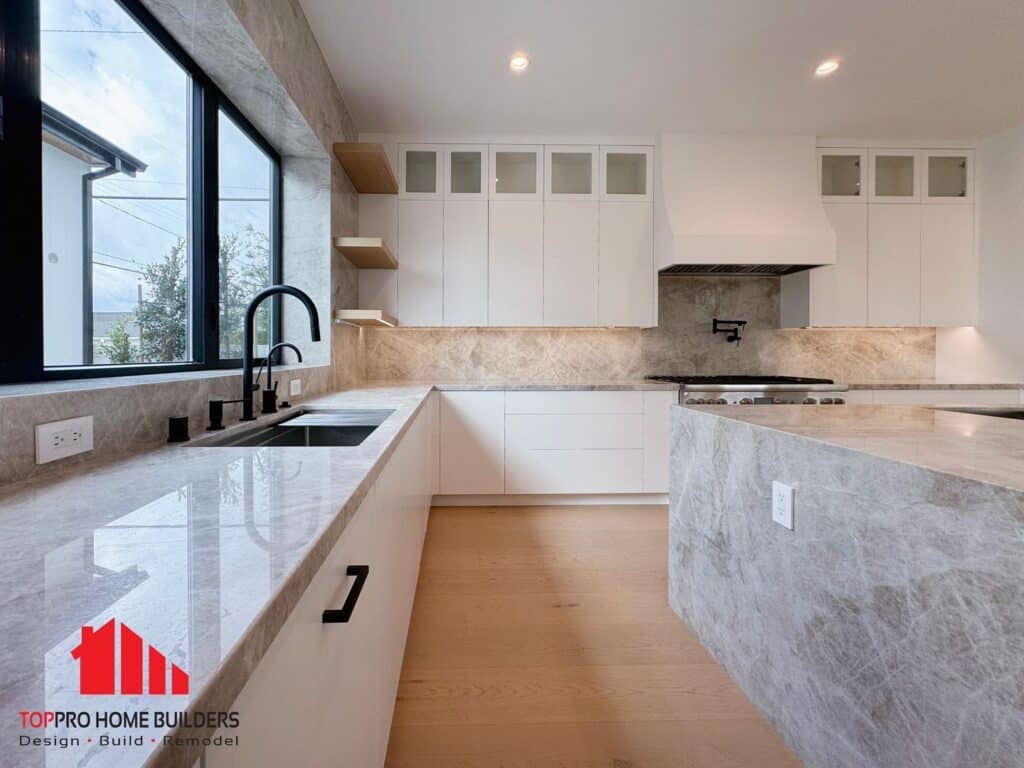 Modern kitchen with marble countertops, white cabinets, and black fixtures.