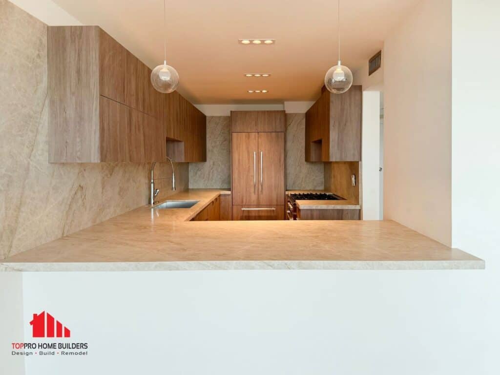 Modern kitchen with wooden cabinets, marble countertops, and pendant lighting.