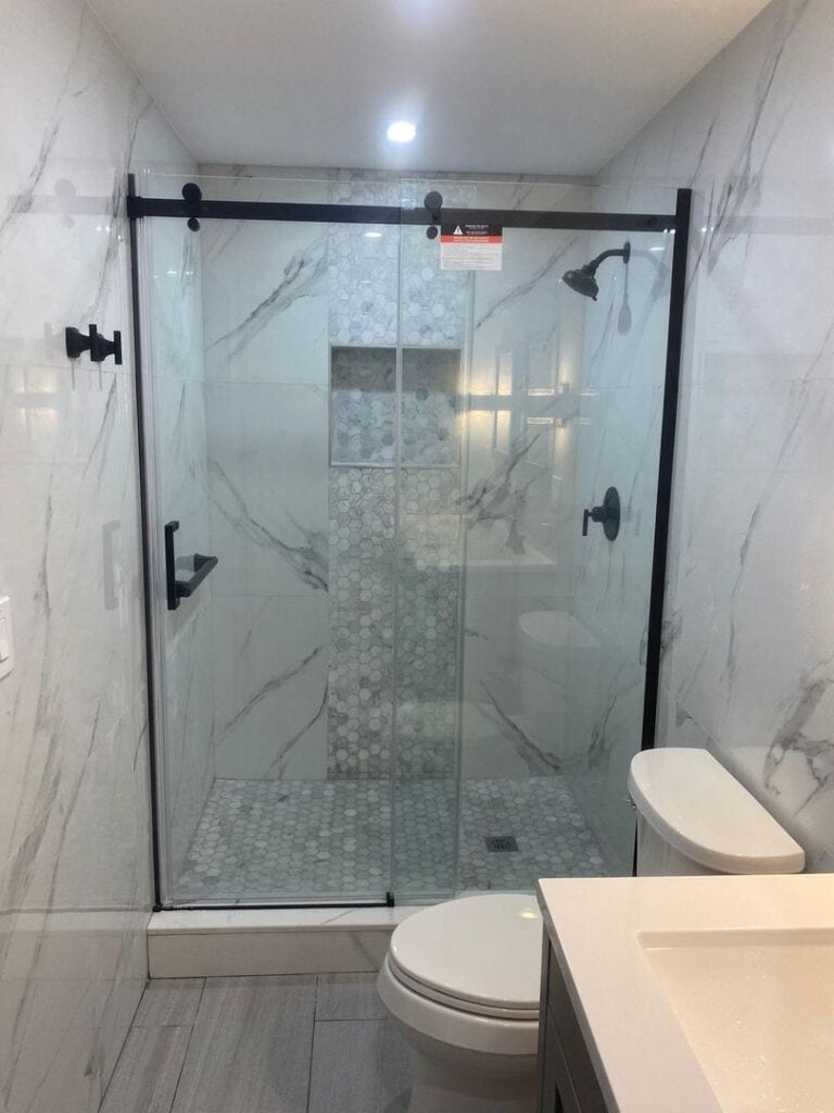 Image of a modern bathroom showcasing a glass shower enclosure and marble-like tiles.