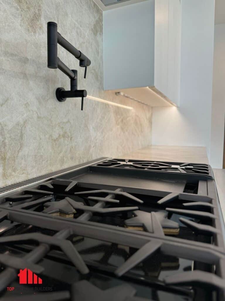 Modern kitchen with black stove grates, pot filler faucet, and white cabinets.