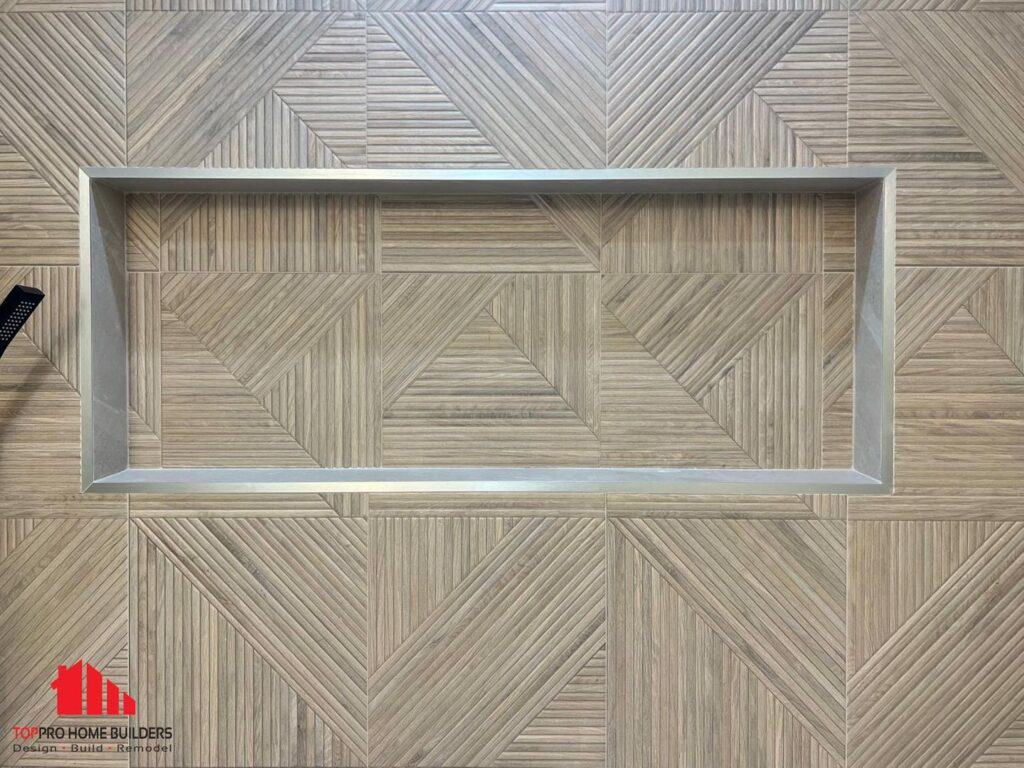 Bathroom wall with geometric tiles and recessed shelf, featuring part of a showerhead.