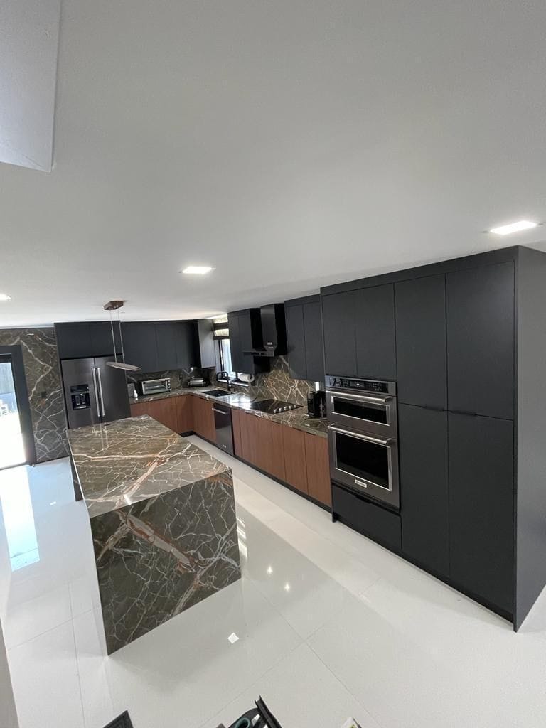 Image of a modern kitchen with dark cabinets, marble island, and stainless steel appliances.