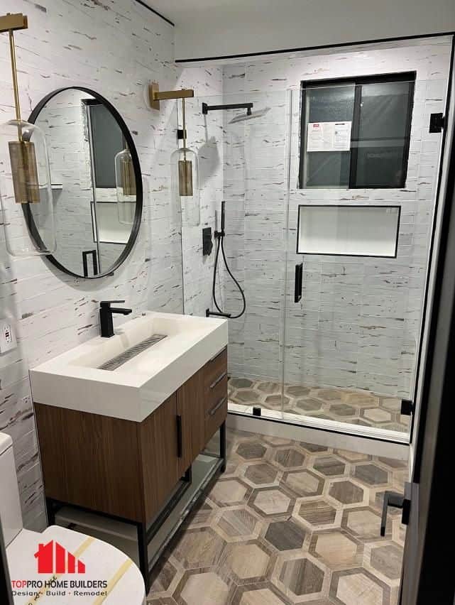 Image of a modern bathroom with glass shower, wooden vanity, and hexagonal tile floor.