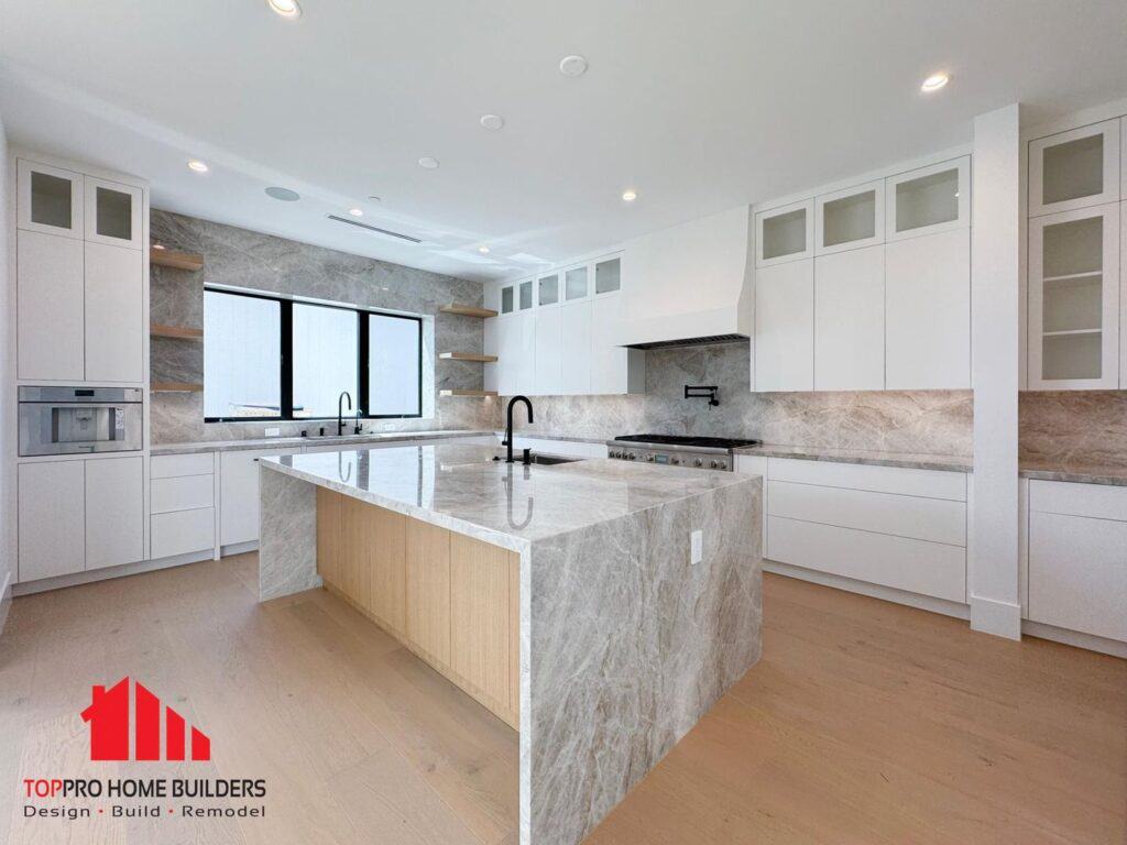 Image of a modern kitchen with a marble island and white cabinets.