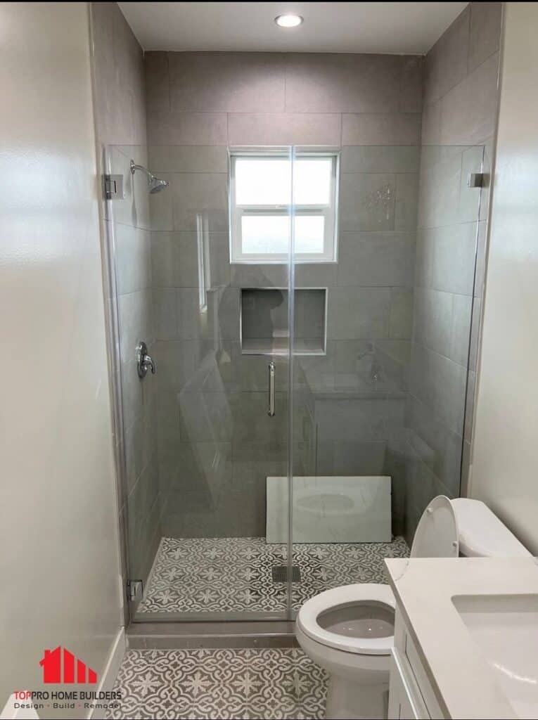 Bathroom with glass shower, gray tiles, patterned floor, and vanity.