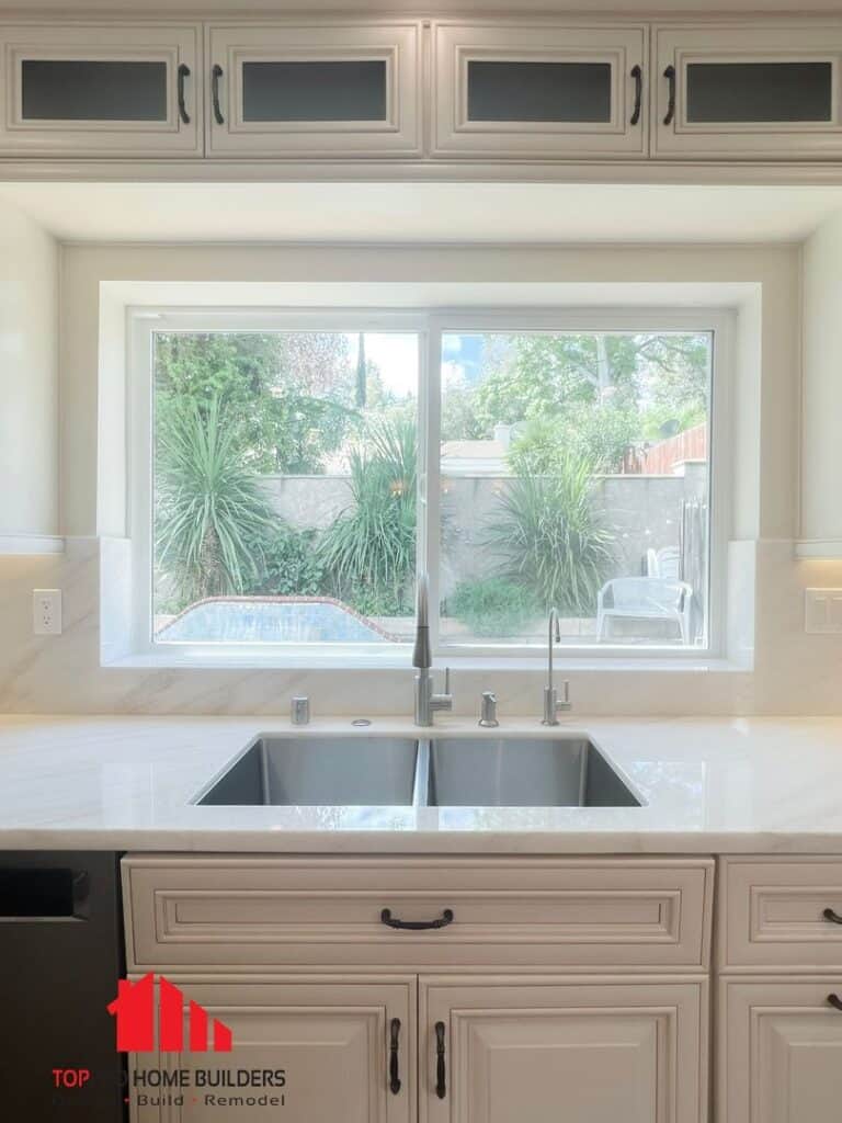 Kitchen sink area with large window overlooking a garden, featuring modern fixtures and cabinetry.