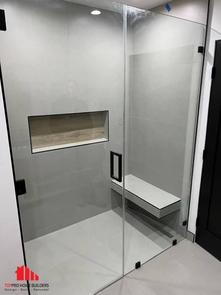 Image of a modern shower with glass doors, floating bench, and recessed shelf in a remodeled bathroom.