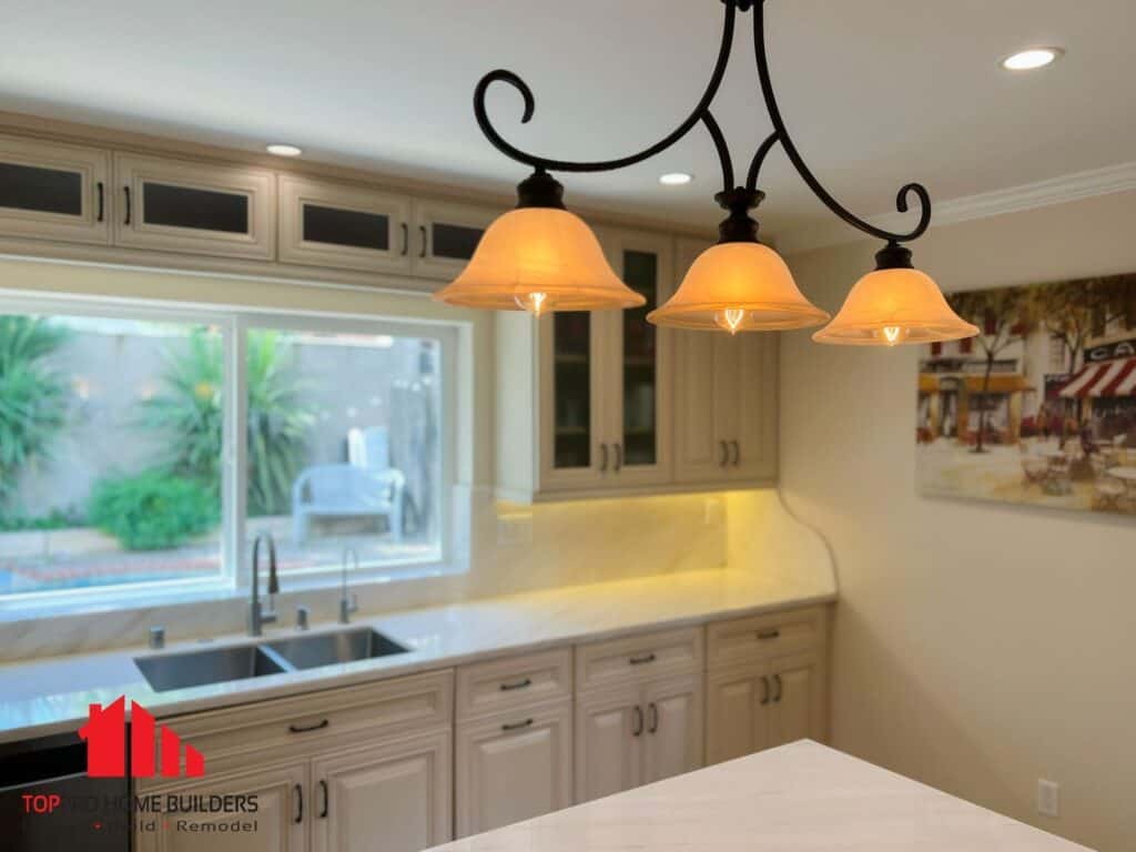 Image of a remodeled kitchen with beige cabinets, marble countertop, and chandelier lighting.